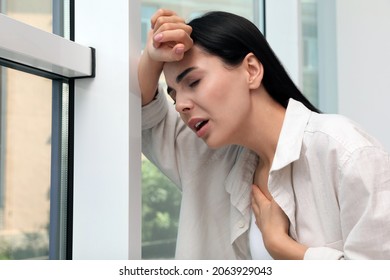 Young woman suffering from breathing problem near window indoors - Shutterstock ID 2063929043
