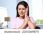 Young woman suffering from ear pain indoors