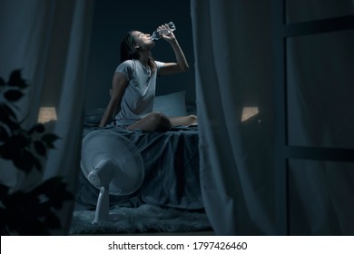 Young woman suffering from insomnia and heat, she is sitting on the bed and drinking fresh water - Shutterstock ID 1797426460