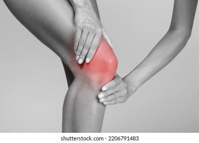 Young Woman Suffering From Knee Pain, Pressing Hands To Sore Spot, Highlighted In Red, Black And White Photo. Inflammation, Arthritis, Trauma, Health Problem And Injury