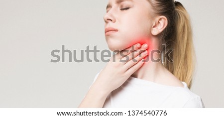 Young woman suffering from pain in throat, touching inflamed zone on her neck, panorama with empty space