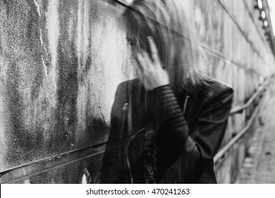 Young woman suffering from a severe disorientation, confusion, or sadness outdoors, in front of a wall. Converted to black and white, grain added, blurry, slightly out of focus. - Shutterstock ID 470241263