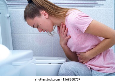 Young Woman Suffers From Nausea And Vomiting Due To Digestive And Stomach Illness Problems At Bathroom. Morning Toxicosis In First Trimester Of Pregnancy. Food Poisoning