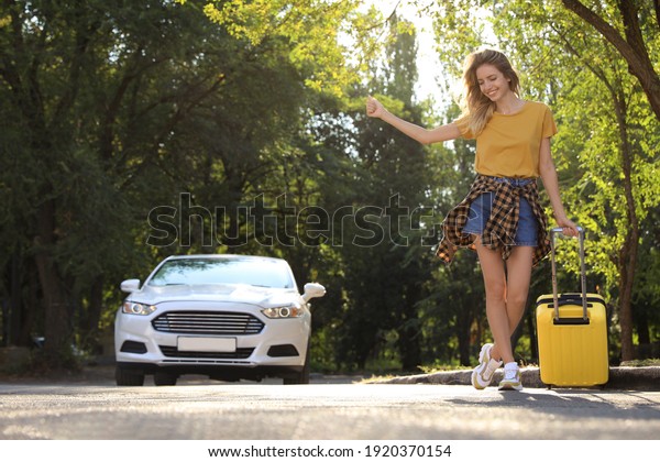 Young\
woman with suitcase catching taxi on city\
street