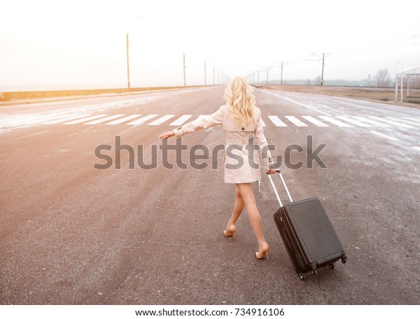 young
woman with suitcase hitch-hiking on a winter
road