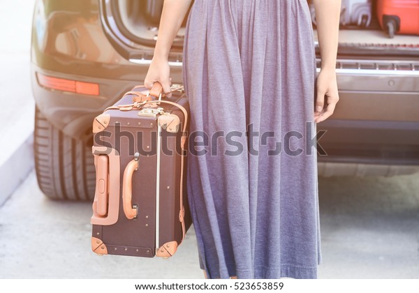 Young woman with\
suitcase near car trunk
