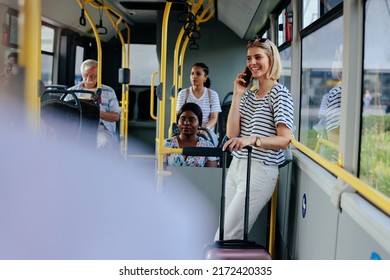 A young woman with a suitcase is riding the shuttle bus and talking on her cellphone - Powered by Shutterstock