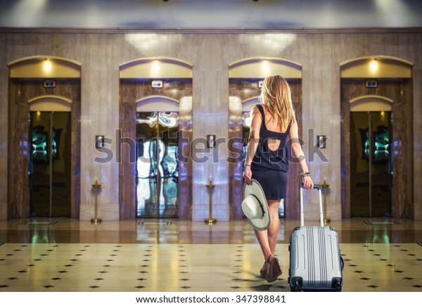 Young\
Woman with suitcase walking at the hotel\
lobby