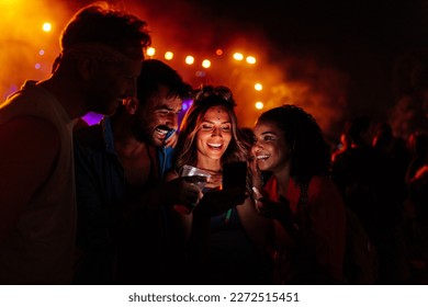 Young woman at summer festival is using  her smartphone with her friends standing next to her watching. - Powered by Shutterstock