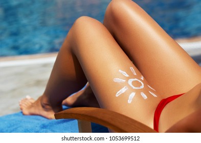 Young Woman With Sun Shape On The Leg Holding Sun Cream Bottle On The Beach. Sun Protection Sun Cream, On Her Smooth Tanned Legs. Sunblock. Skincare. 