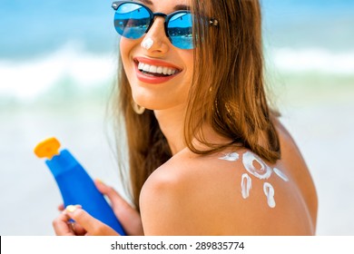 Young woman with sun shape on the shoulder holding sun cream bottle on the beach 