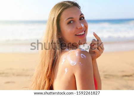 Young woman with sun shape on the shoulder applying sun cream protection on her nose on the beach