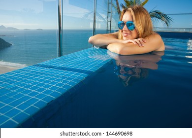 Young Woman Sunbathing By The Pool On The Roof Of The Penthouse In Rio De Janeiro On Copacabana Beach Background