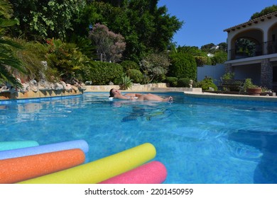 Young Woman Sunbathing And Keeping Cool, Floating In Swimming Pool In A Mediterranean Garden