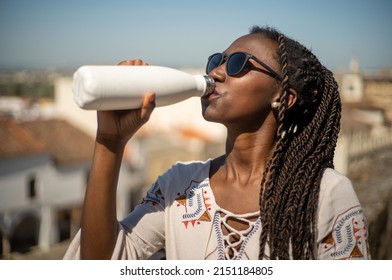 Young woman with sunglasses drinking water from a reusable bottle in a sunny day - Shutterstock ID 2151184805