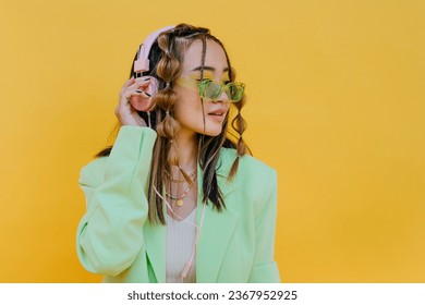 Young woman with sunglasses listening music on headphones against yellow background