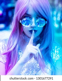 Young woman with sunglasses in neon lights holding finger on lips
