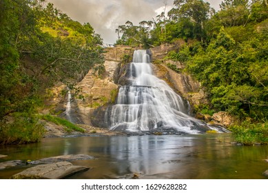 Young woman in a Sunny day in the Tropical waterfall falls from the mountain cliff to the jungle, serene landscape of Diyaluma falls.
