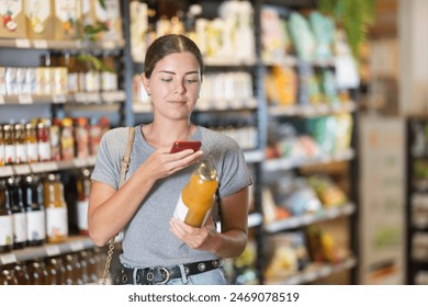 Young woman in supermarket scan QR code bottle of drink. Girl buyer photo information on packaging of bio product.