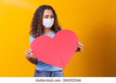 young woman in surgical mask holding a huge paper heart with space for text. - Powered by Shutterstock