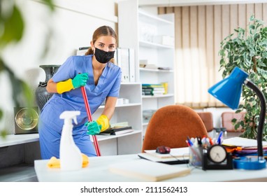 Young Woman In Surgical Scrubs And Face Mask Cleaning Floor. She's Using Mop And Rubber Gloves.