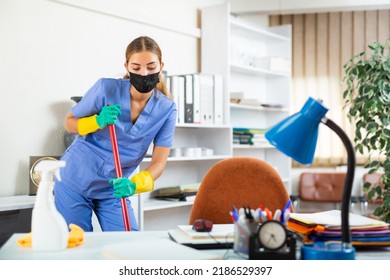 Young Woman In Surgical Scrubs And Face Mask Cleaning Floor. She's Using Mop And Rubber Gloves.