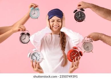 Young woman surrounded by loud alarm clock on pink background