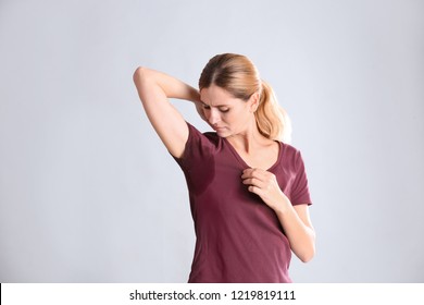 Young woman with sweat stain on her clothes against light background. Using deodorant