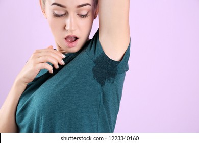 Young woman with sweat stain on her clothes against color background, space for text. Using deodorant