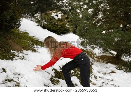 A young woman in a sweater collects snow for a snowball during a snowball game. Concept of winter entertainment and outdoor activities, New Year's celebration