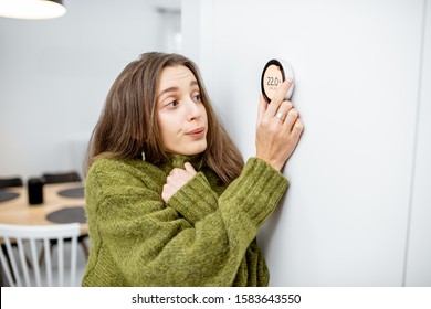 Young Woman In Sweater Feeling Cold, Waiting For The House To Heat Up, Controlling Heating System With A Smart Home Thermostat