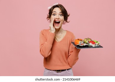 Young Woman In Sweater Hold Makizushi Sushi Roll Served On Black Plate Traditional Japanese Food Scream Hot News About Sales Discount With Hands Near Mouth Isolated On Plain Pastel Pink Background.