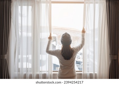 young woman in sweater looking through the window in winter season, happy female rising arms and stretching after waking at apartment or home in the morning. Lifestyle and Relaxing concepts - Powered by Shutterstock