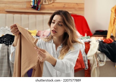 Young Woman With Sweater In Messy Room. Fast Fashion Concept