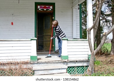 Young Woman Sweeps Front Porch Of Balcony With Broom