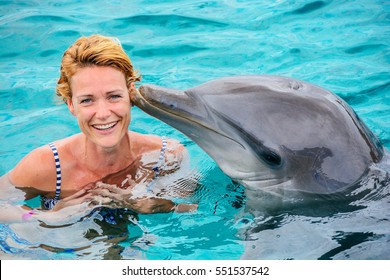 Young woman swimming with dolpin at a dolfinarium on a sunny day.