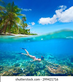 Young Woman Swimming On The Bright Coral Reef In The Sea On A Background Of A Tropical Beach