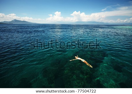 Young woman swimming over coral reef in transparent tropical sea. Bunaken island. Indonesia