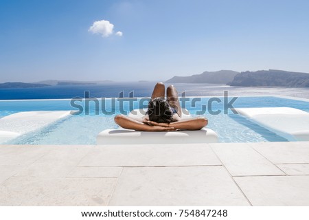 young woman in the swimming pool ,infinity pool relaxing looking out over the ocean caldera of Oia Santorini Greece