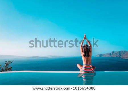 young woman in the swimming pool relaxing looking out over the ocean caldera of Oia Santorini Greece,Woman relaxing in infinity swimming pool looking over the sea 