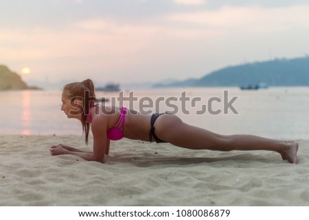 Young woman in swimsuit exercising on beach stretching her legs during sunset at sea. Fitness girl doing exercises on seashore