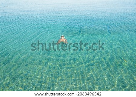 Young woman in a swimsuit and hat swimming in sea waves near the beach. View from above. Top, drone view