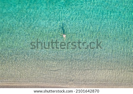 Young woman in a swimsuit and hat swimming in sea waves near the beach. View from above. Top, drone view
