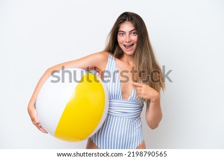 Young woman in swimsuit holding beach ball isolated on white background with surprise facial expression