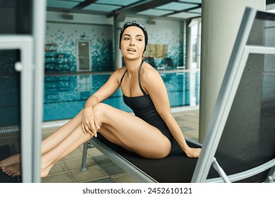 A young woman in swimsuit and swim cap sitting peacefully on a lounge chair in an indoor swimming pool. - Powered by Shutterstock