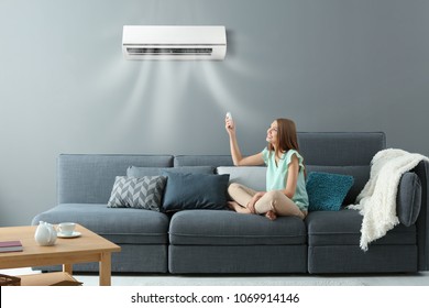 Junge Frau, die die Klimaanlage einschaltet, während sie zu Hause auf dem Sofa sitzt