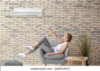 Young Woman Switching On Air Conditioner While Sitting In Armchair At Home