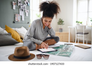 Young woman with tablet and map indoors at home, planning traveling trip.