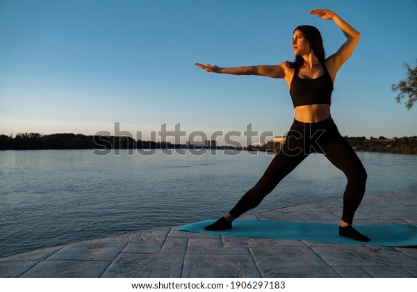 Young woman in Tai Chi pose, outdoors in by the\
river, energy balance and vitality\

