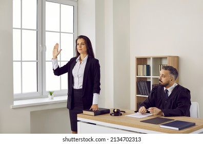 Young Woman Takes An Oath Before Giving A Sworn Testimony During The Court Trial. Crime Witness Standing By The Judge In The Courtroom Swears On The Holy Bible That She Will Tell Nothing But The Truth